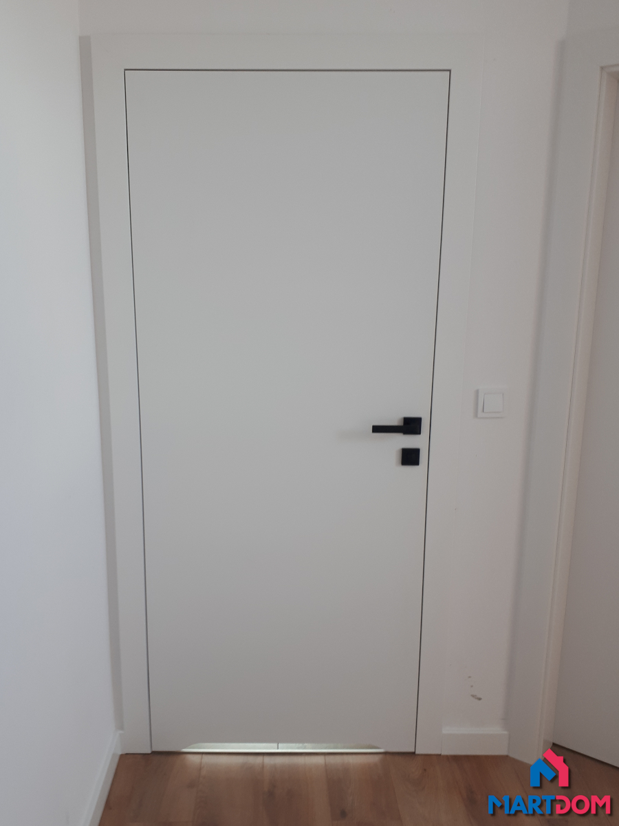 Białe drzwi wewnętrzne białe ściany dre uni lakierowane podcięcie drzwi do łazienki z widokiem od korytarza jasna podłoga zamek wc