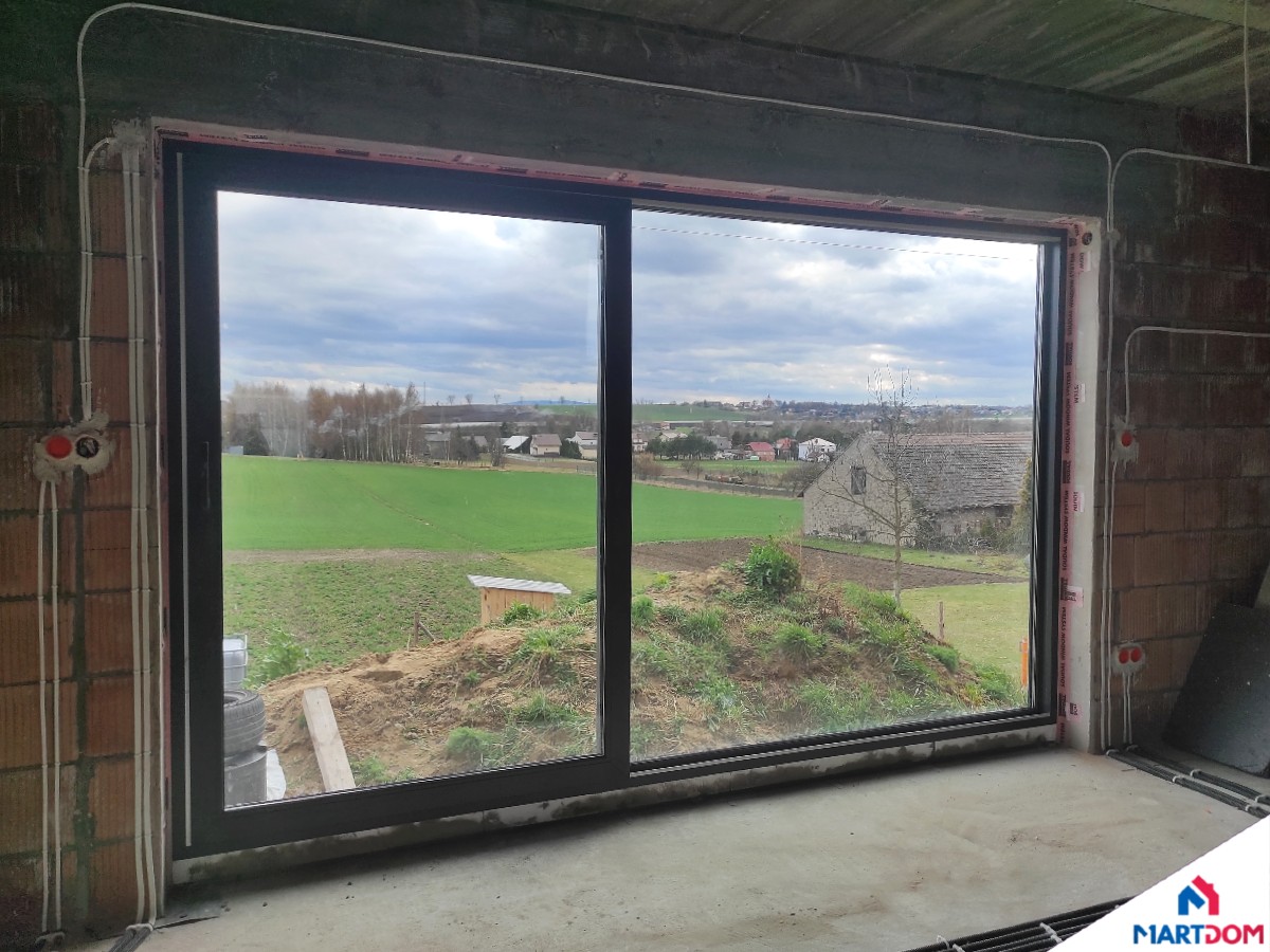 Okno przesuwne okno plastikowe okno smart Slide niesymetryczne antracytowe okno od wewnątrz z widokiem na podwórko w trakcie budowy montaż na taśmach