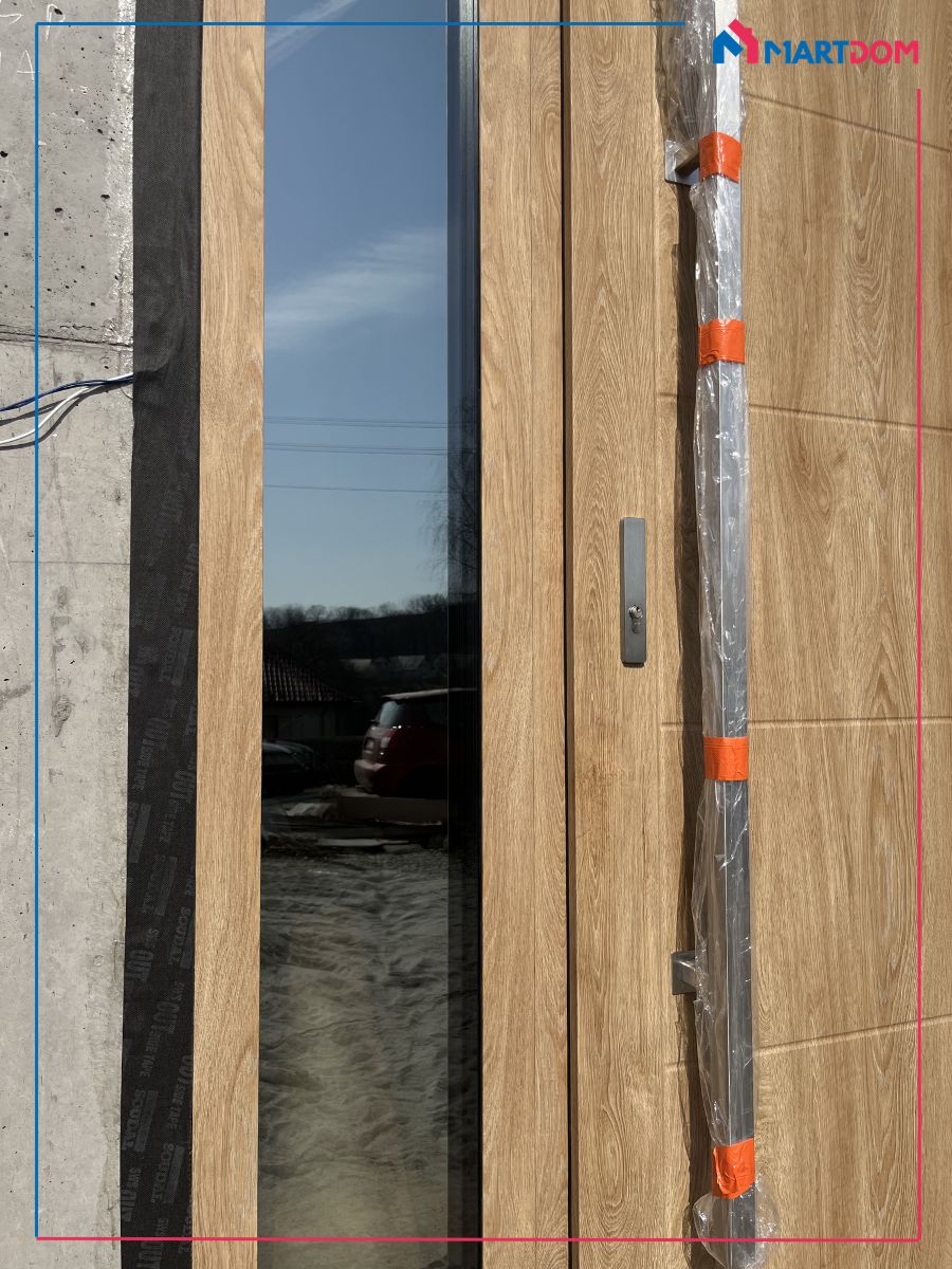 Szyba reflex brąz widok od zewnątrz efekt odbicia zbliżenie na antabę inox i doświetle boczne w kolorze Turner Oak owoczesnymi przetłoczeniami tworzy spójną całość z antabą i naświetlem bocznym. Szyba reflex brąz pozwala w dużej mierze zakryć to, co dzieję się w środku, dając jednocześnie pełen wgląd w to, co dzieje się na zewnątrz.